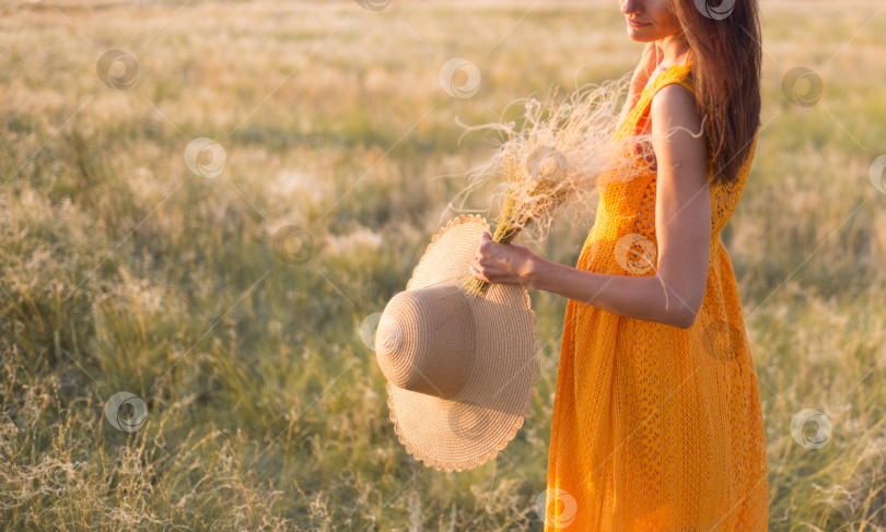 Скачать Красивая романтичная девушка на природе. Вид сзади на красивую девушку, одетую в повседневное оранжевое платье, с соломенной шляпой в руках на поле в лучах солнца. Развевает длинные волосы. Осень. Сияй, солнышко. теплый оттенок с подсветкой. фотосток Ozero