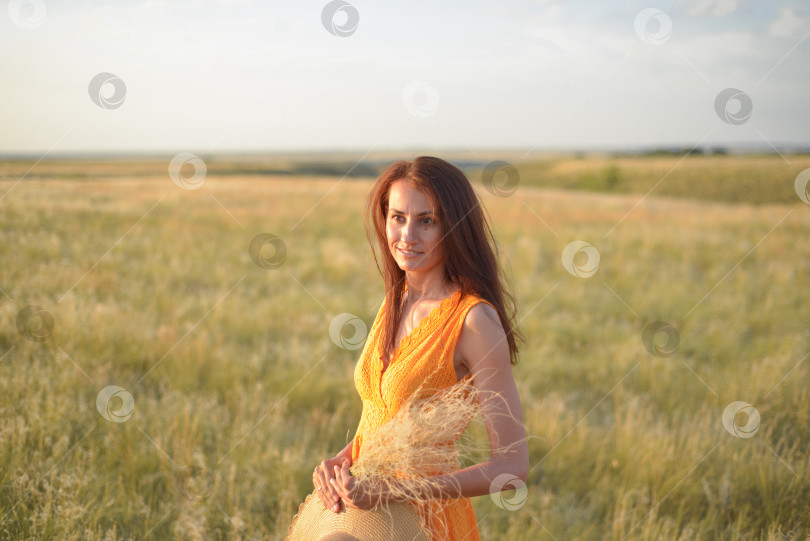 Скачать Симпатичная молодая девушка с длинными каштановыми волосами в оранжевом платье в поле на закате. Концепция свободы и природы фотосток Ozero