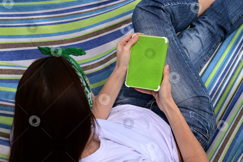 Скачать Молодая счастливая женщина, сидящая в парке на зеленой траве на природе с телефоном в руках, в повседневной одежде и общающаяся по видеосвязи, концепция здоровой рекреационной медитации фотосток Ozero