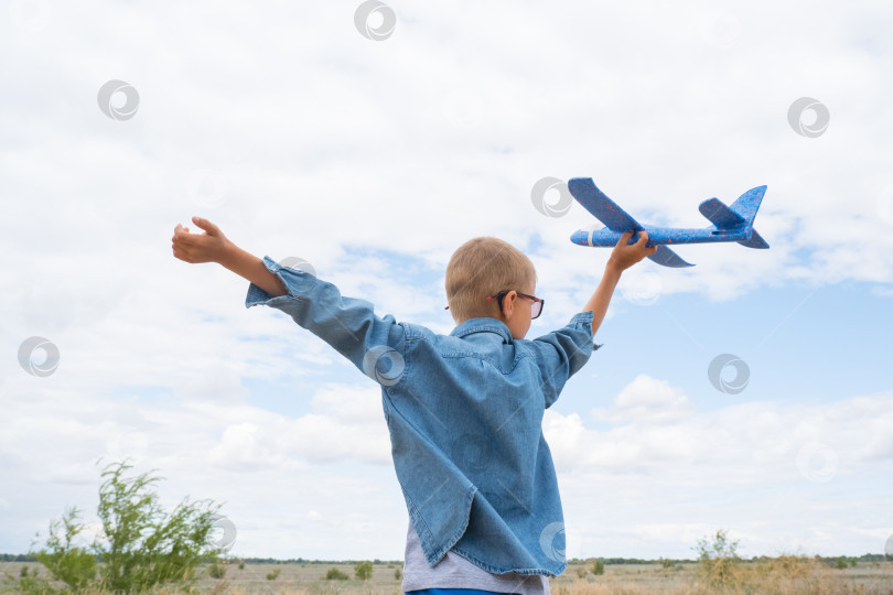 Скачать Счастливый ребенок играет с игрушечным самолетиком на фоне голубого неба в открытом поле фотосток Ozero