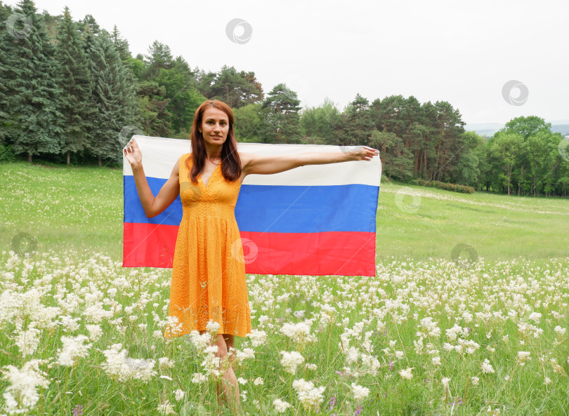 Скачать Молодая женщина в желтом платье с государственным флагом России на открытом воздухе в цветущем поле. фотосток Ozero