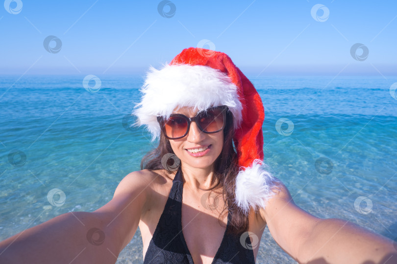 Скачать Концепция Рождества и праздников - Красивая женщина в шляпе Санты делает селфи на берегу моря фотосток Ozero