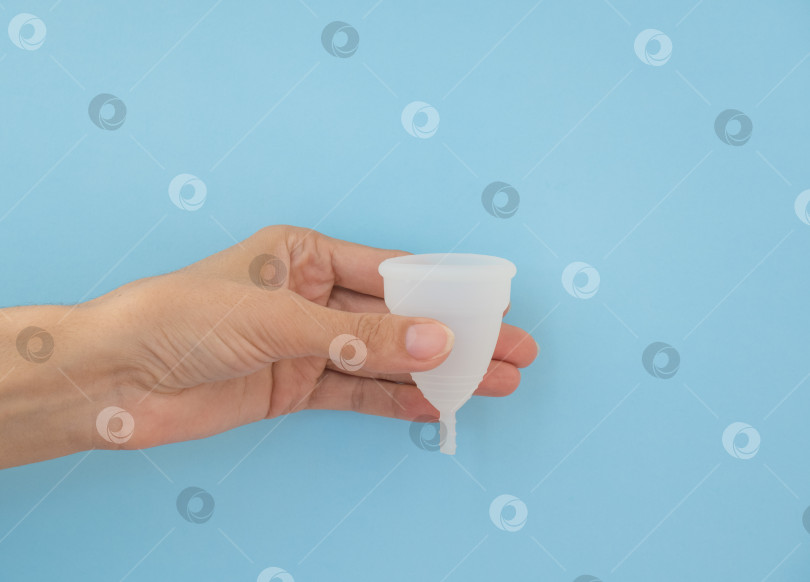 Скачать Крупным планом женская рука, держащая менструальную чашу, на синем фоне. Концепция женского здоровья, альтернативы без отходов фотосток Ozero