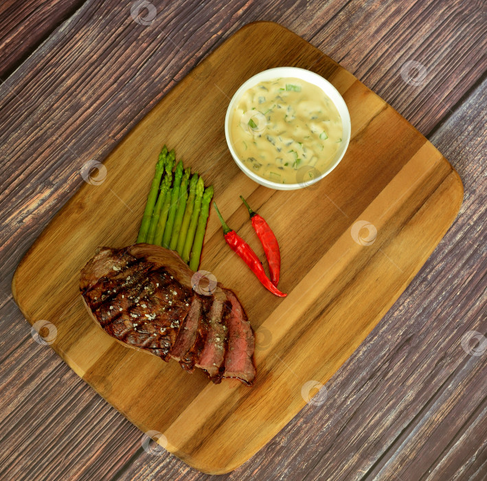 Скачать Деревянная тарелка с кусочком жареной говяжьей вырезки со спаржей, острым перцем и соусом. фотосток Ozero