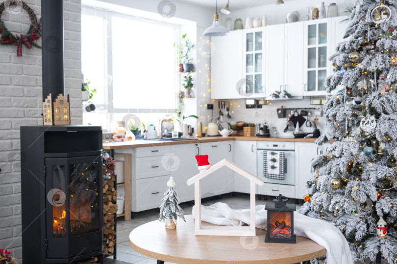 Скачать Рождественский декор на белой кухне с горящей плитой-камином, праздничный беспорядок, деревенский интерьер с заснеженной елкой. Новый год, рождественское настроение, уютный дом. фотосток Ozero