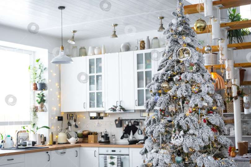 Скачать Праздничный рождественский декор на белой кухне, современный деревенский интерьер со снежной елкой и гирляндами. Новый год, рождественское настроение, уютный дом, металлическая модульная лестница. Общий план фотосток Ozero
