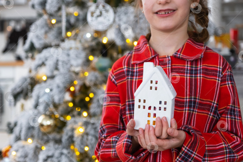 Скачать Счастливый ребенок с крошечным домиком в уютном доме с рождественским декором праздничной белой кухни. Подарок на Новый год. Страхование, переезд в новый дом, ипотека, аренда и покупка недвижимости фотосток Ozero