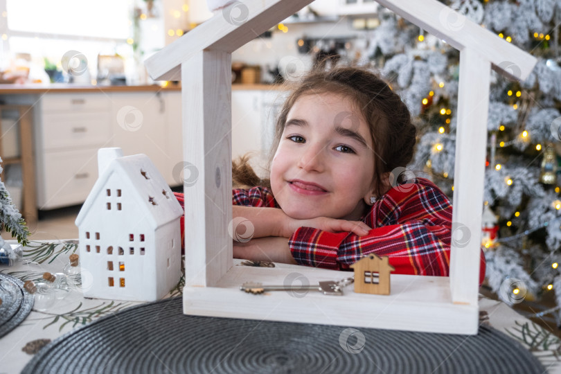 Скачать Счастливый ребенок с крошечным домиком в уютном доме с рождественским декором праздничной белой кухни. Подарок на Новый год. Страхование, переезд в новый дом, ипотека, аренда и покупка недвижимости фотосток Ozero
