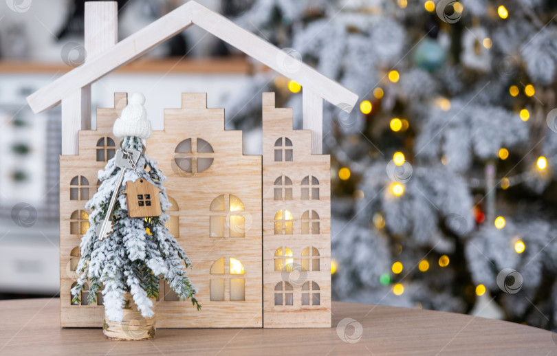 Скачать Ключ на рождественской елке и крошечный домик в уютном доме с рождественским декором на столе праздничной белой кухни. Подарок на Новый год. Страхование, переезд в новый дом, ипотека, аренда и недвижимость фотосток Ozero