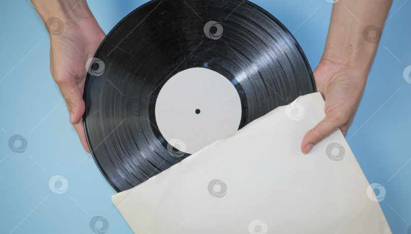 Скачать Руки держат старую виниловую пластинку в старом бумажном футляре на светло-голубом фоне. фотосток Ozero