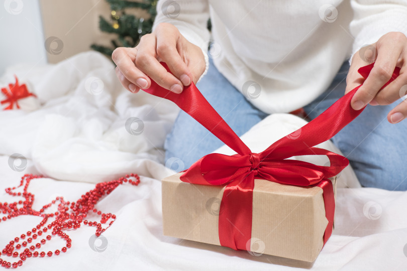 Скачать счастливых праздников! Женские руки развязывают бант на подарочной коробке к Рождеству в белой постели. фотосток Ozero
