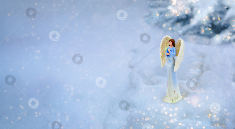 Скачать Рождественский ангел с книгой в руке в снегу возле рождественской елки вечером. Фото природы на открытом воздухе. Снежная погода фотосток Ozero