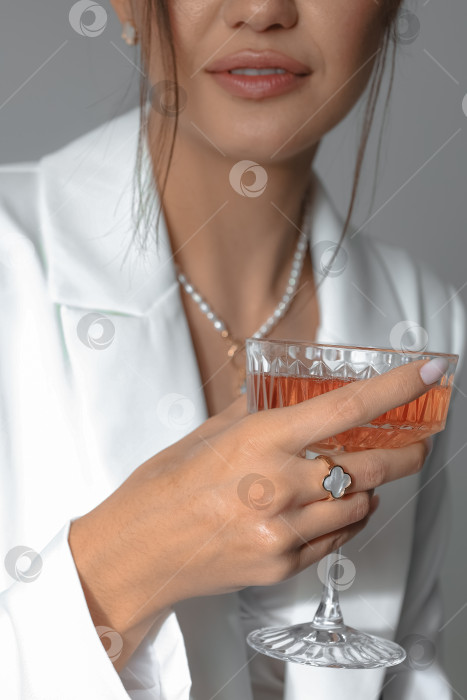 Скачать Стильная молодая женщина в современном белом блейзере, с бокалом для коктейля в руке и кольцом на пальце фотосток Ozero