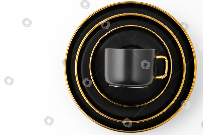 Скачать Набор черных и золотистых керамических тарелок и чашек на белом фоне. Вид сверху фотосток Ozero