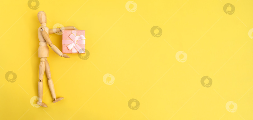Скачать Деревянная фигурка в розовой подарочной коробке. Желтый фон, место для копирования фотосток Ozero