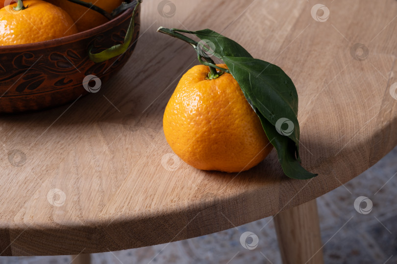 Скачать Несколько свежих спелых мандаринов с листьями лежат на столе с деревянной спинкой. Избирательный подход. фотосток Ozero