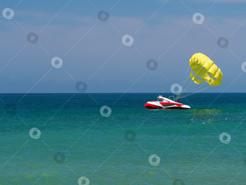 Скачать На море штиль. Вдалеке на бирюзовой глади воды стоит лодка. К лодке прикреплен парашют для парасейлинга. Морской пейзаж с лодкой и парашютом. Свободное место для текста. фотосток Ozero