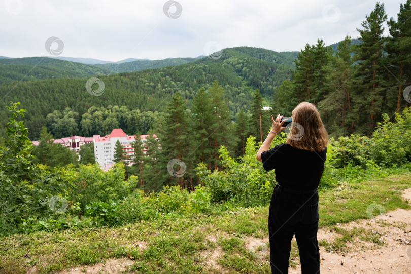 Скачать Красивая путешествующая женщина, стоящая на вершине горы на закате и пользующаяся мобильным телефоном. Туристическая тропа в высокогорье. Цифровая связь. фотосток Ozero