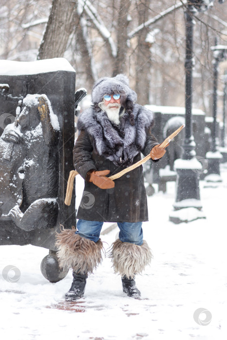 Скачать Пожилой седовласый мужчина с пышными усами и бородой смотрит вдаль и улыбается. Портрет пожилого стильного хипстера крупным планом в меховой шапке и шубе. Рождество фотосток Ozero