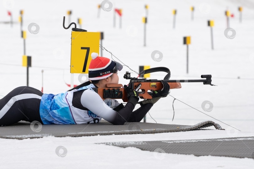 Скачать Спортсменка-биатлонистка Чхве Юна, Южная Корея, стреляет из винтовки в положении лежа. Биатлонистка на стрельбище юниорских соревнований по биатлону East Cup фотосток Ozero