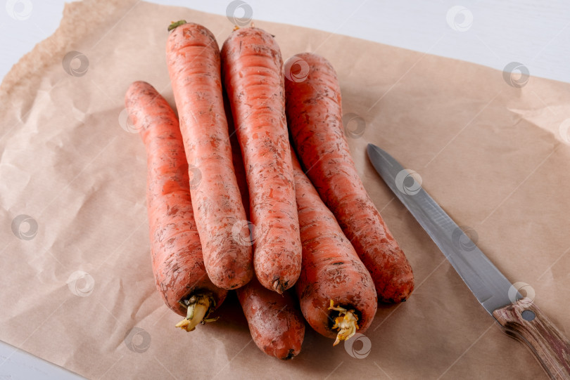 Скачать Свежая сырая морковь лежит на пергаментной бумаге на кухонном столе. Выборочный фокус. фотосток Ozero