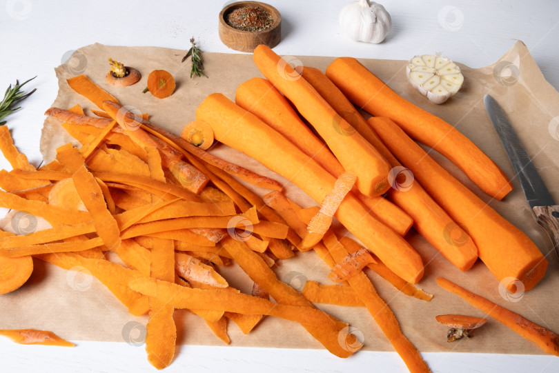 Скачать Очищенная свежая сырая морковь лежит на пергаментной бумаге на кухонном столе. Выборочный фокус. фотосток Ozero