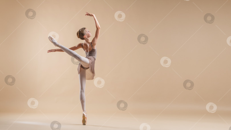 Скачать Красивая молодая девушка- профессиональная студентка-балерина в пуантах и трико на светло-бежевом фоне. фотосток Ozero