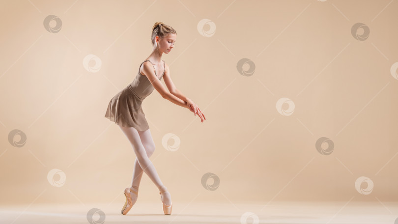 Скачать Красивая молодая девушка- профессиональная студентка-балерина в пуантах и трико на светло-бежевом фоне. фотосток Ozero