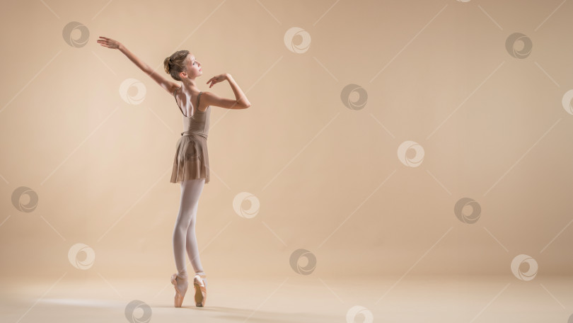 Скачать Красивая молодая девушка, профессиональная студентка-балерина, в пуантах и трико на светло-бежевом фоне. фотосток Ozero