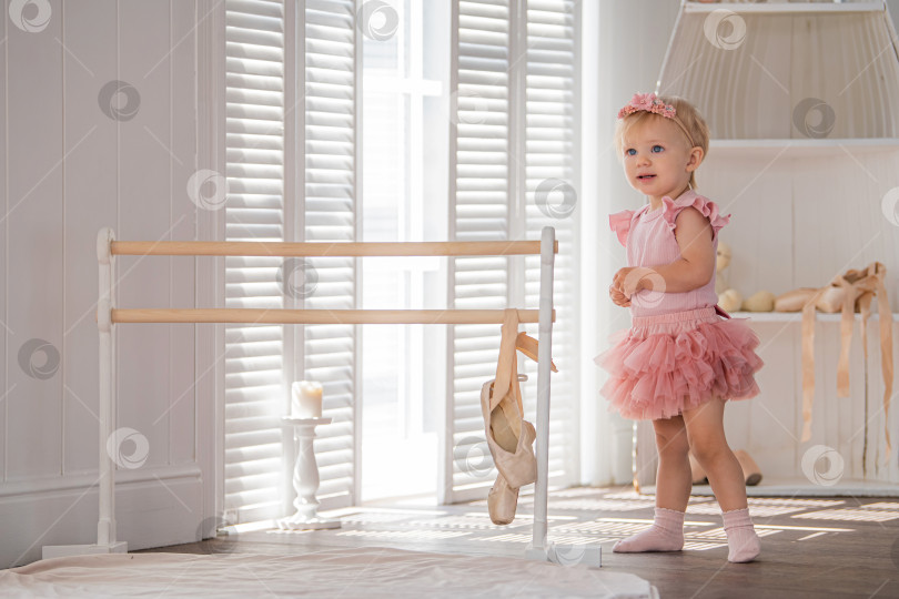 Скачать Симпатичная маленькая балерина в розовом балетном костюме стоит у станка в комнате. Ребенок и балетный танец. Copyspace. фотосток Ozero