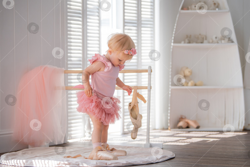 Скачать Симпатичная маленькая балерина в розовом балетном костюме стоит у станка в комнате. Ребенок и балетный танец. Copyspace. фотосток Ozero
