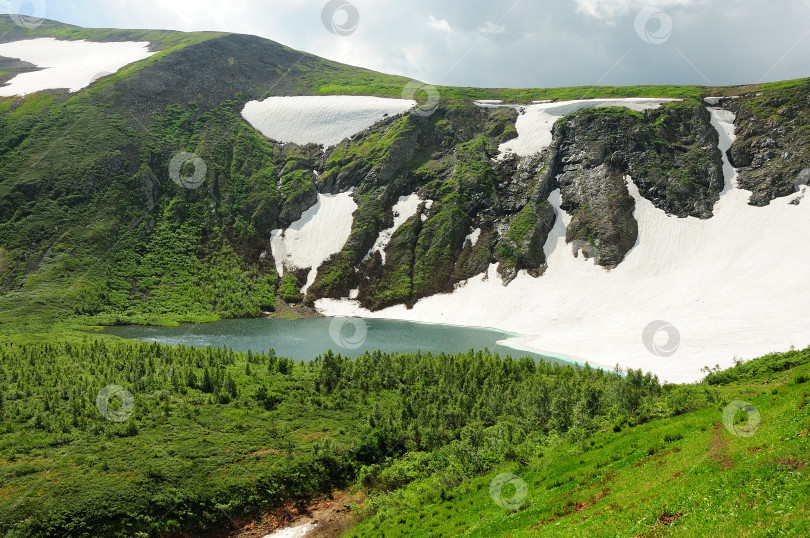 Скачать Тропинка через низкие кусты к красивому озеру в межгорной котловине у подножия холма со снежными склонами. фотосток Ozero