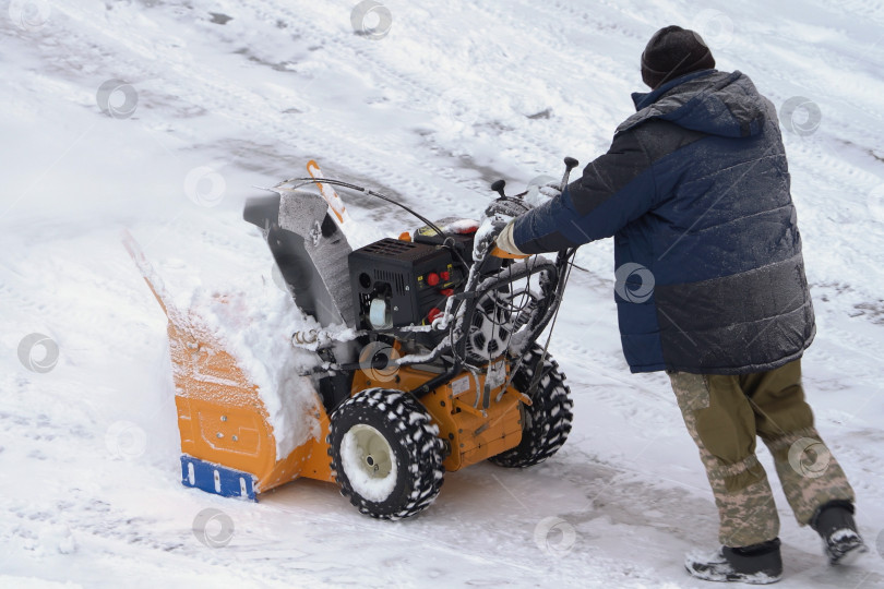 Скачать Мужчина использует снегоуборочную машину для уборки снега после зимней грозы. Ему помогает снегоуборочная машина на зимней дороге фотосток Ozero