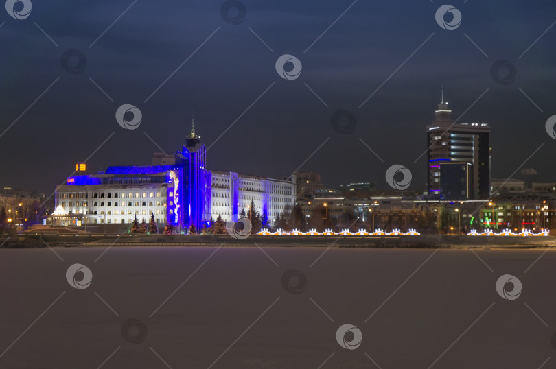 Скачать Казань, Татарстан, Россия – 26 декабря 2023:  Ночной вид города через застывшее озеро Кабан фотосток Ozero