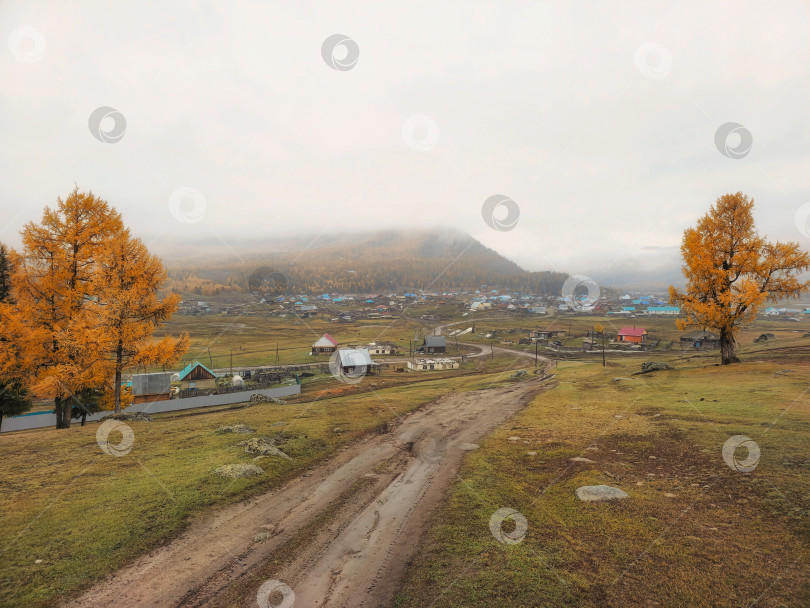 Скачать Осенняя грунтовая дорога с холма в отдаленную деревню. фотосток Ozero
