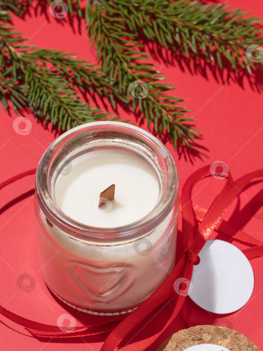 Скачать Ароматическая свеча с ванилью в открытой стеклянной банке и еловой веткой на красном фоне фотосток Ozero