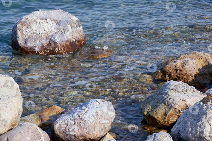 Скачать Мертвое море. Иордания. Крупный план. Кристаллы соли на огромных валунах вдоль побережья. Крупный план. Каменные пляжи вдоль побережья Мертвого моря омываются спокойными изумрудными водами. Штиль на море. фотосток Ozero