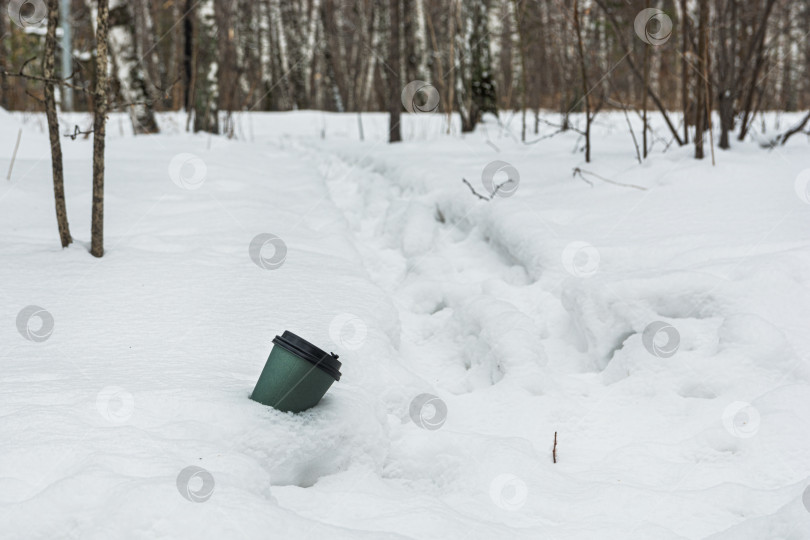Скачать Использованную кофейную чашку выбрасывают в сугроб в зимнем лесу. Концепция загрязнения окружающей среды бытовыми отходами фотосток Ozero
