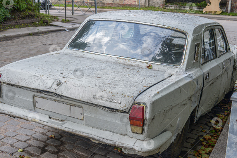 Скачать Старый ржавый белый автомобиль "Волга" стоит на брусчатой дороге фотосток Ozero