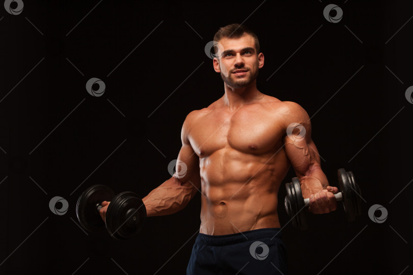 Скачать Красивый спортивный мужчина в тренажерном зале накачивает мышцы с помощью гантелей в тренажерном зале. Фитнес-мускулистое тело, выделенное на темном фоне. фотосток Ozero
