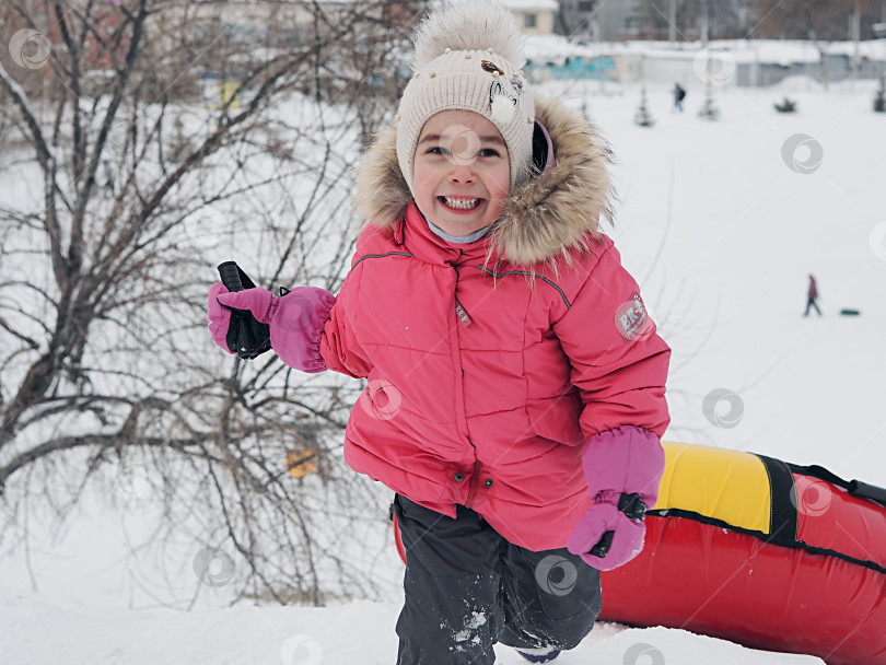 Скачать Девушка взбирается на гору по снегу, на спуске катается на резиновых трубах. Ясный морозный зимний день. фотосток Ozero