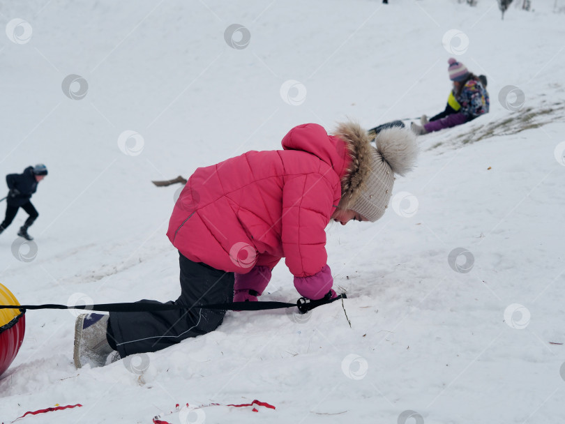 Скачать Девушка взбирается на гору по снегу, на спуске катается на резиновых трубах. Ясный морозный зимний день. фотосток Ozero