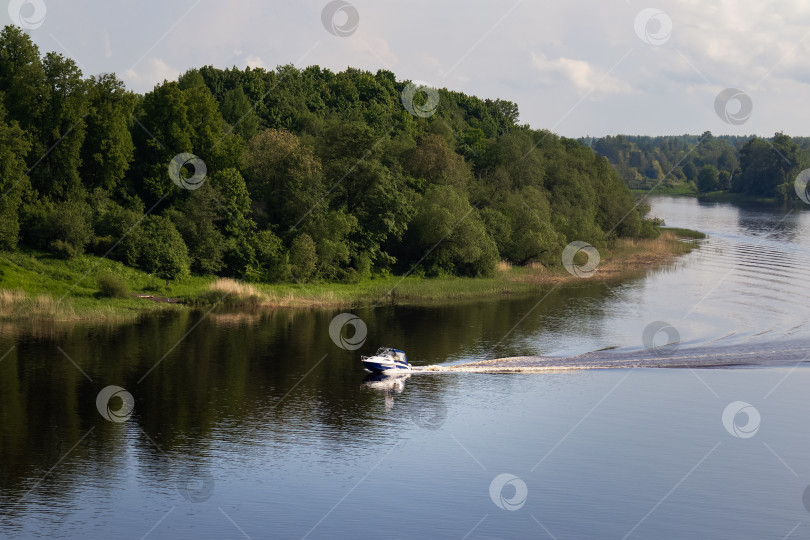 Скачать Моторная лодка плывет по реке на фоне берега с густыми зелеными деревьями фотосток Ozero