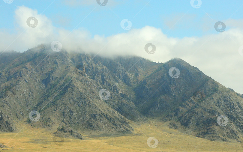 Скачать Высокий скалистый массив с облаками на вершинах и огромным лугом у подножия. фотосток Ozero