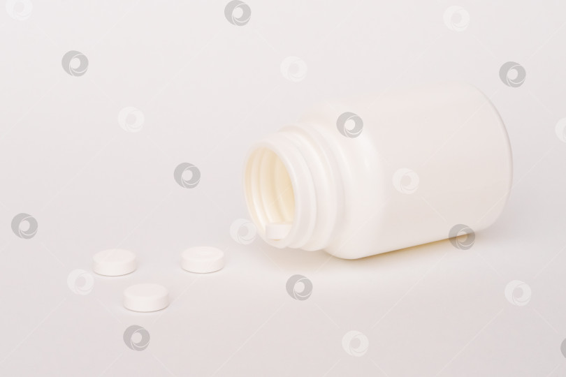 Скачать Белые таблетки высыпаются из пузырька на белое. Лекарство в белых таблетках фотосток Ozero