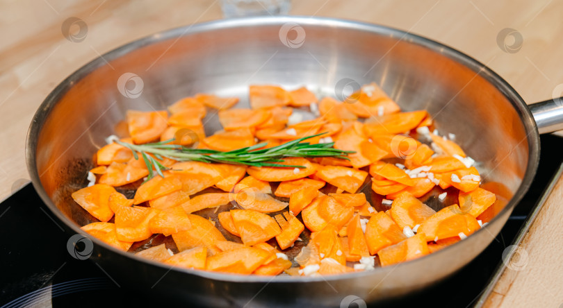 Скачать Обжаривание нарезанной моркови со свежим розмарином на сковороде фотосток Ozero