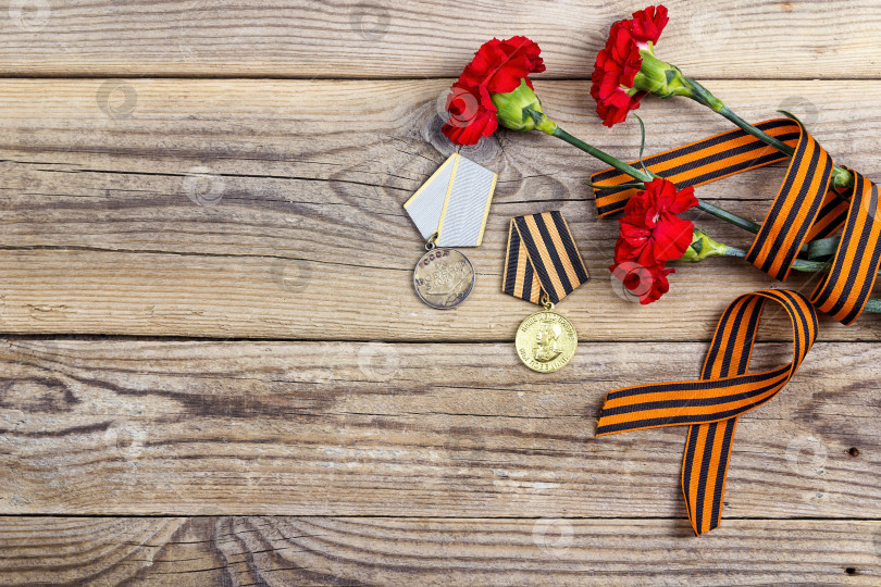 Скачать Медали Великой Отечественной войны, Георгиевская лента и красные гвоздики на деревянном фоне. фотосток Ozero