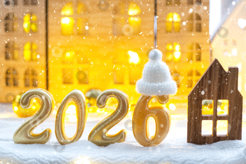 Скачать Золотые цифры № 2026 и крошечный домик на фоне уютных окон дома с теплым светом и праздничным декором из звезд, снега и гирлянд. Поздравительная открытка, С Новым годом, уютный дом фотосток Ozero
