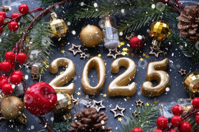 Скачать Золотые фигурки 2025 года, выполненные из свечей на фоне черного каменного сланца, украшены праздничным декором из звезд, блесток, еловых веток, шаров и гирлянд. Поздравительная открытка "с Новым годом". фотосток Ozero