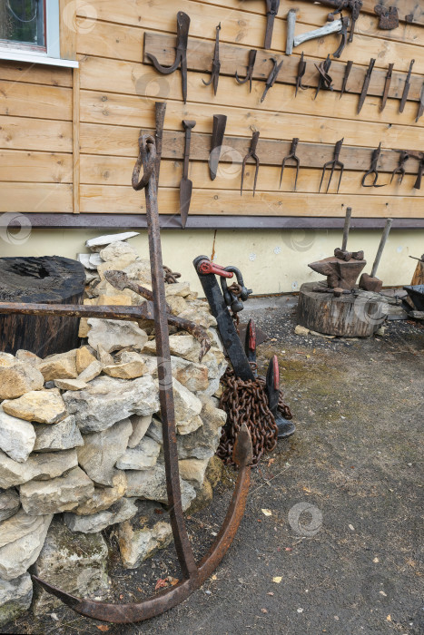 Скачать Старинный железный якорь на фоне старинных металлических инструментов на деревянной стене. фотосток Ozero